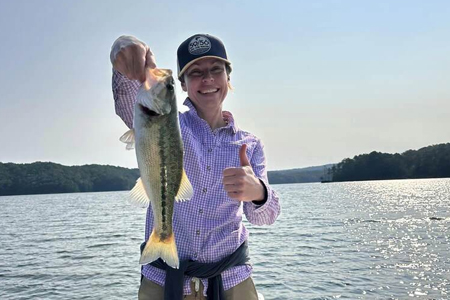  Young woman on boat holds up fish caught on lake.