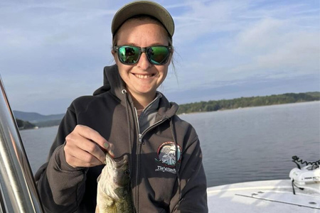 Woman holds up fish caught by open mouth.