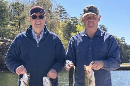  Two gentlemen hold up four fish caught on lake fishing trip.