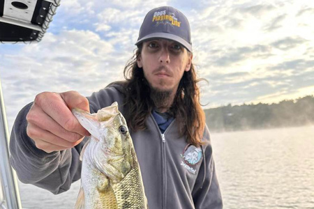  Man holds up fish caught by open mouth.