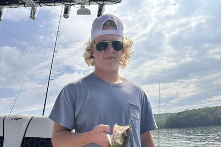  Young adult holds up fish caught on lake.