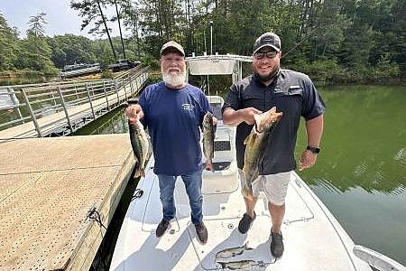 Father and son pose with fish caught on bow of boat. 