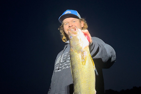  Young man holds up fish caught during night fishing trip.